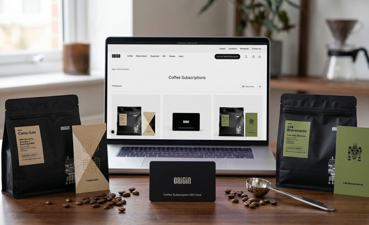 Origin Coffee subscription bags, gift card, and laptop on a wooden desk with scattered coffee beans